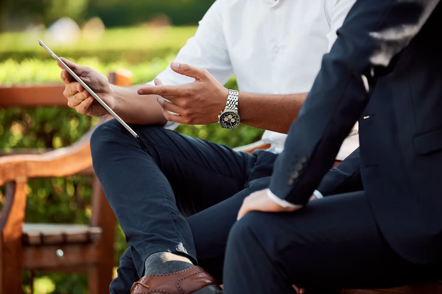 Deux hommes assis sur un banc dans un jardin échangent autour d'une tablette